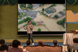 A man demonstrates his lecture with custom climate change video in the background